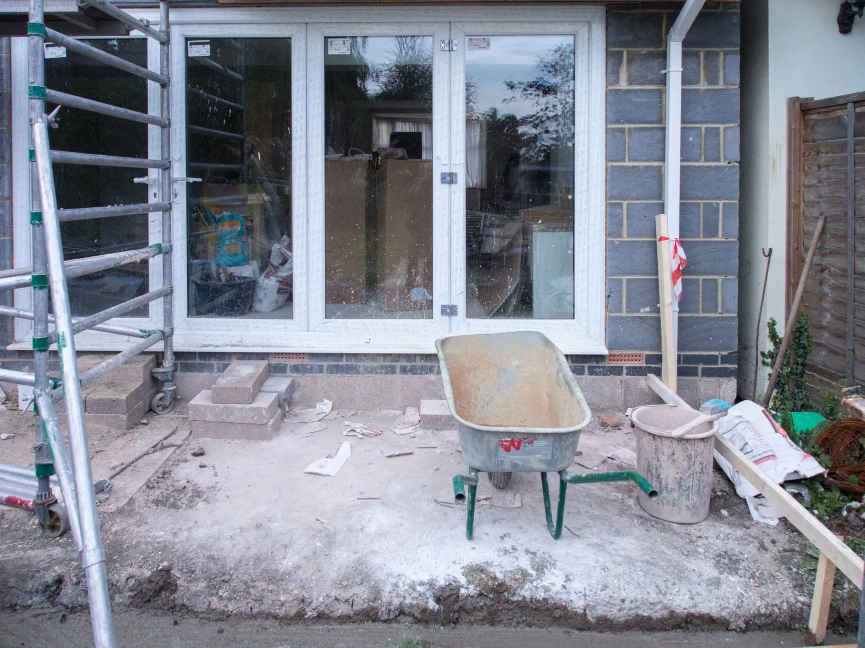 Extension de maison en blocs béton en chantier, baie vitrée posée et brouette sur la dalle