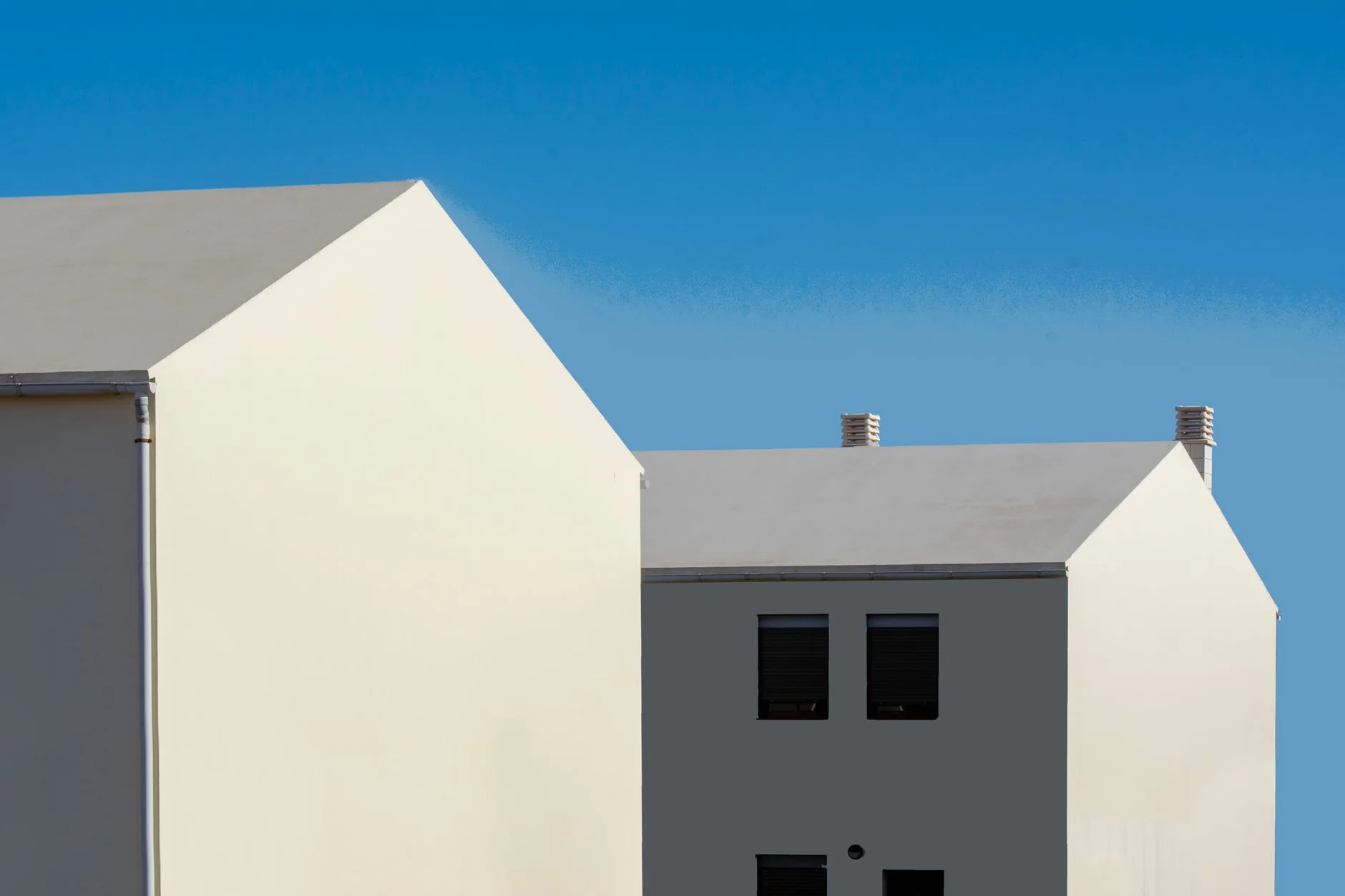 Maisons minimalistes aux volumes simples, façades blanches et toits à deux pentes